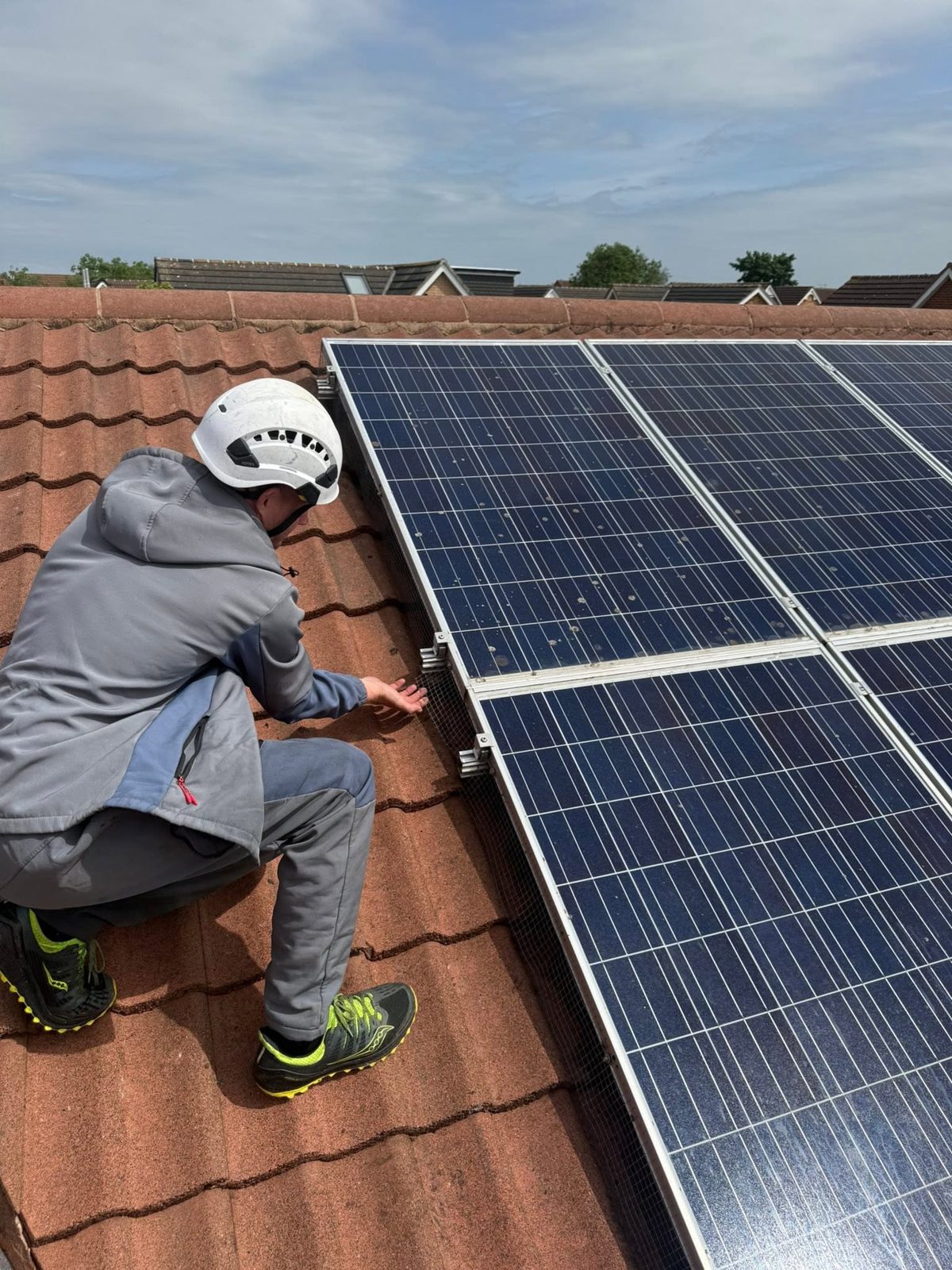 IGM operative in helmet and workwear fitting mesh around solar panels on a roof in Teesside
